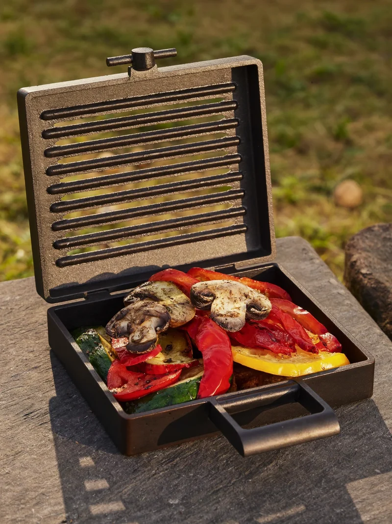 Grille en fonte et panier garni de poivrons, courgettes et champignons sur ardoise